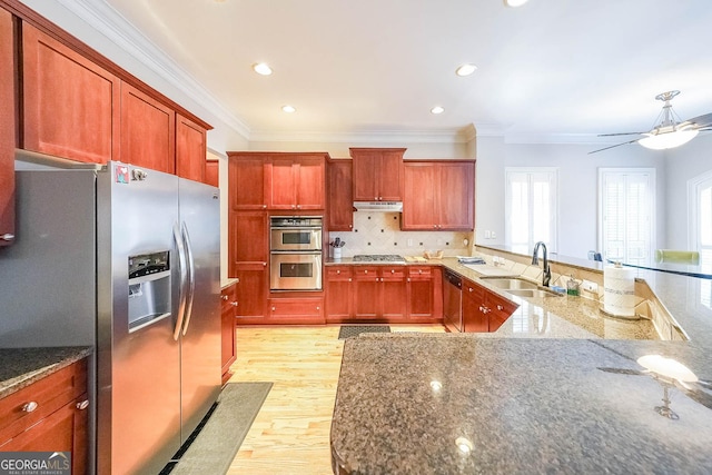 kitchen with stainless steel appliances, backsplash, a sink, dark stone counters, and under cabinet range hood