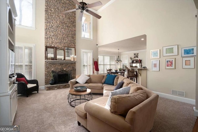 carpeted living room with ceiling fan, a stone fireplace, a healthy amount of sunlight, and a high ceiling