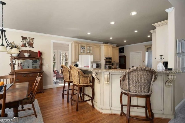 kitchen with decorative light fixtures, kitchen peninsula, cream cabinets, and light wood-type flooring