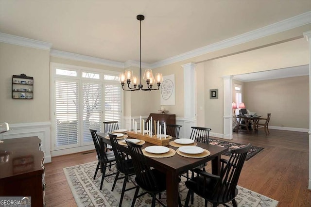 dining area featuring crown molding, a notable chandelier, dark wood-type flooring, and ornate columns