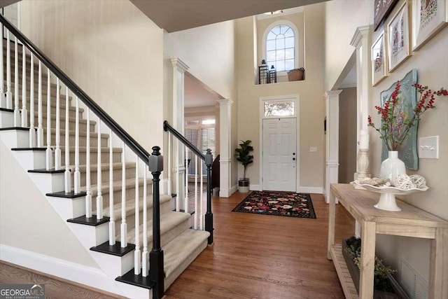 foyer with wood-type flooring, a high ceiling, and ornate columns