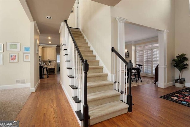 staircase featuring hardwood / wood-style floors, a high ceiling, and ornate columns