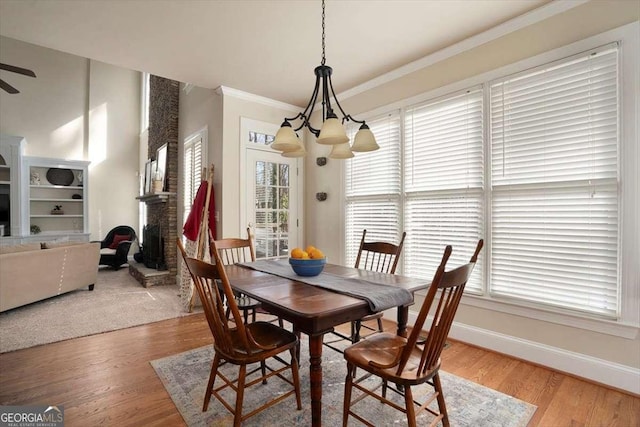 dining room featuring ornamental molding, wood-type flooring, ceiling fan with notable chandelier, and a fireplace