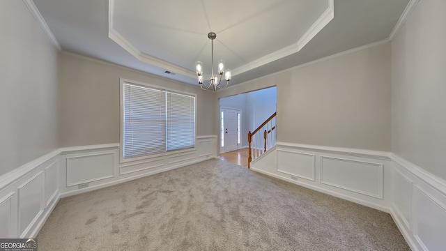 spare room featuring a chandelier, light colored carpet, ornamental molding, and a raised ceiling