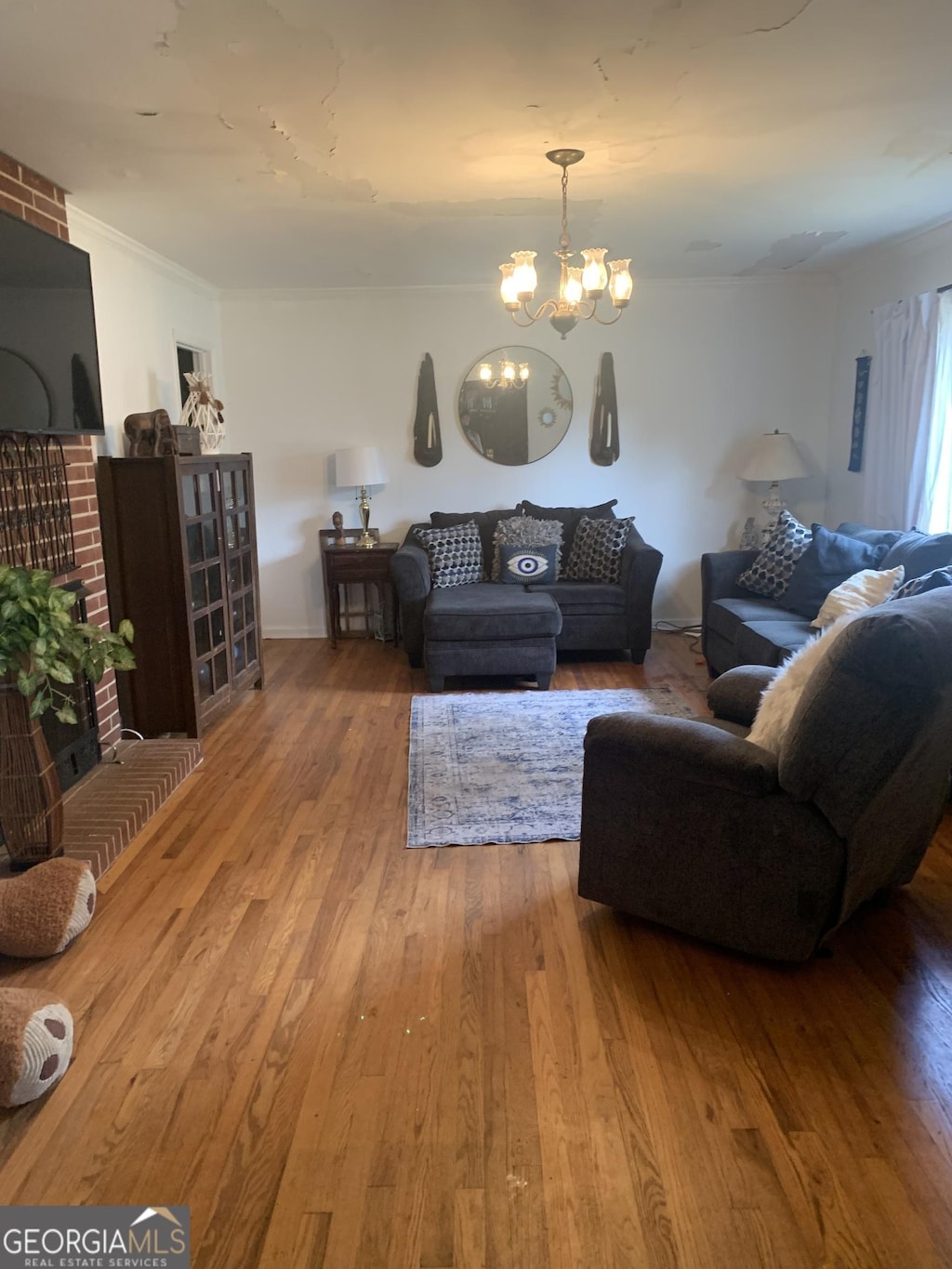 living room with hardwood / wood-style flooring, ornamental molding, a brick fireplace, and an inviting chandelier