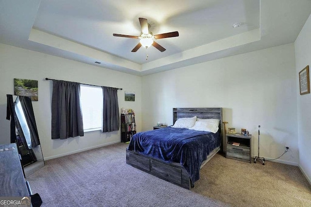 bedroom with a raised ceiling, carpet floors, and ceiling fan