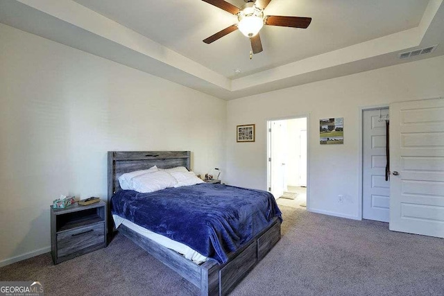 carpeted bedroom with a raised ceiling and ceiling fan