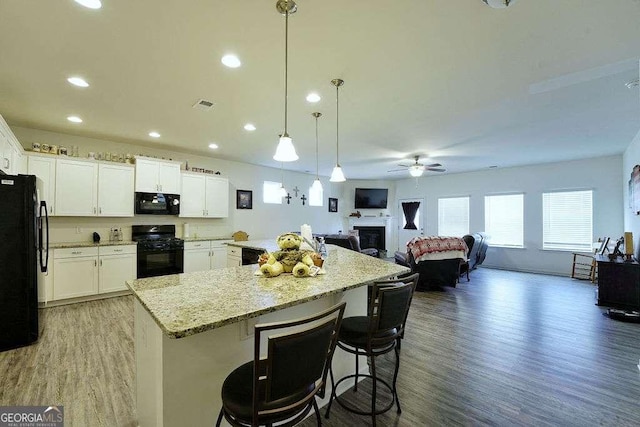 kitchen with white cabinetry, pendant lighting, a kitchen bar, and black appliances