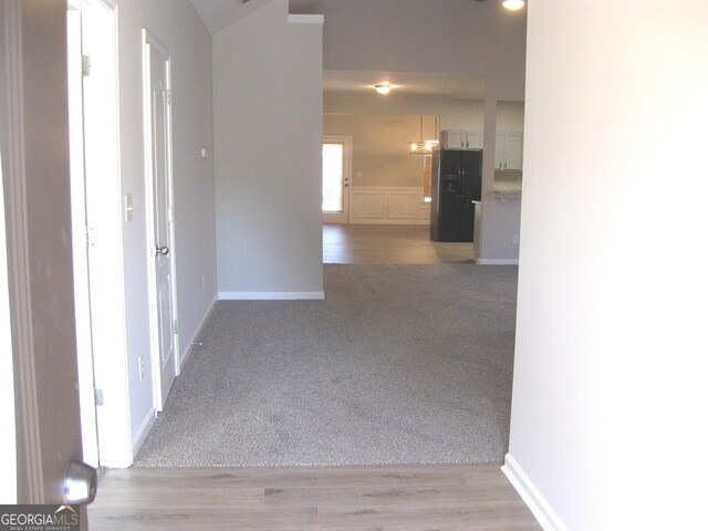 kitchen with high vaulted ceiling, white cabinetry, light colored carpet, kitchen peninsula, and black refrigerator with ice dispenser