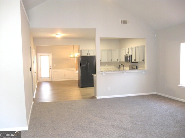 kitchen with high vaulted ceiling, white cabinets, light carpet, black refrigerator with ice dispenser, and kitchen peninsula