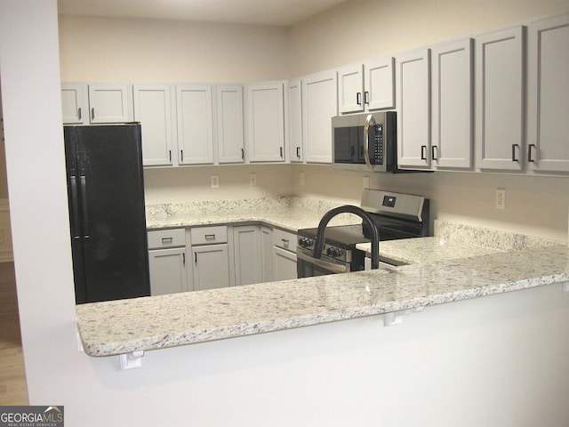 kitchen with white cabinetry, appliances with stainless steel finishes, light stone counters, and kitchen peninsula