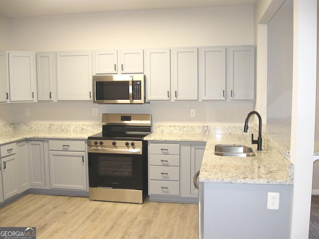 kitchen featuring sink, gray cabinetry, light stone counters, light hardwood / wood-style flooring, and appliances with stainless steel finishes