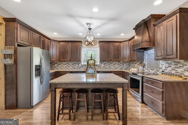 kitchen with hanging light fixtures, stainless steel appliances, a center island, light stone countertops, and custom range hood