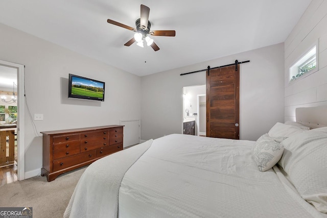 bedroom featuring ceiling fan, ensuite bath, a barn door, and light carpet