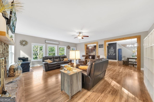 living room featuring a stone fireplace, ceiling fan with notable chandelier, and light wood-type flooring