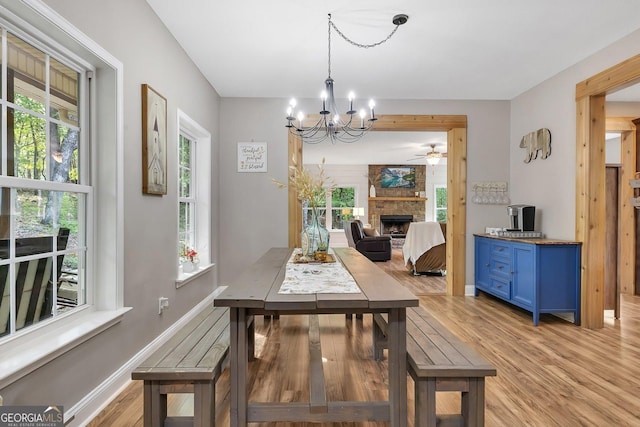 dining area with an inviting chandelier, a stone fireplace, and light hardwood / wood-style floors