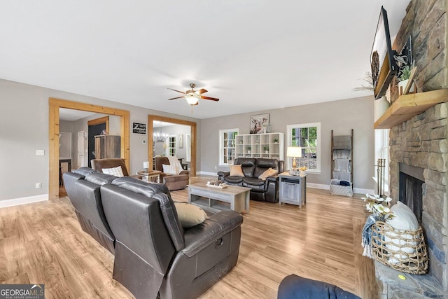 living room featuring ceiling fan, a stone fireplace, and light wood-type flooring