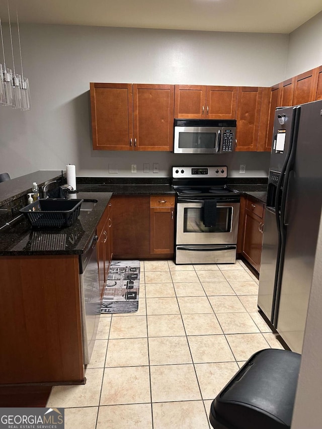 kitchen with dark stone countertops, appliances with stainless steel finishes, hanging light fixtures, and light tile patterned floors