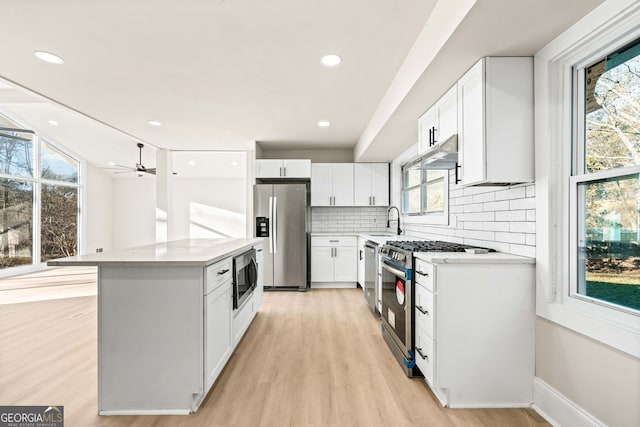 kitchen featuring appliances with stainless steel finishes, tasteful backsplash, white cabinetry, a center island, and light wood-type flooring