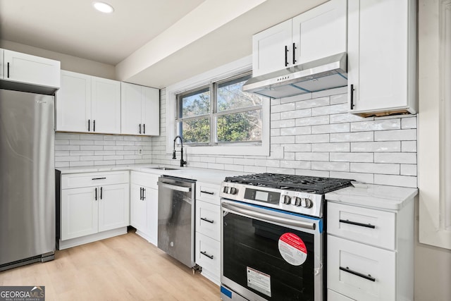 kitchen with appliances with stainless steel finishes, white cabinetry, sink, light stone counters, and light hardwood / wood-style floors