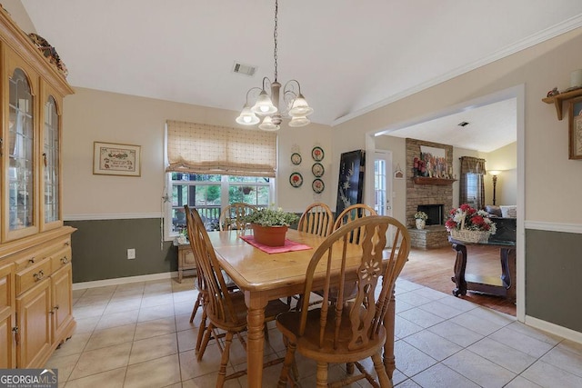 dining space with a fireplace, a chandelier, vaulted ceiling, and light tile patterned floors