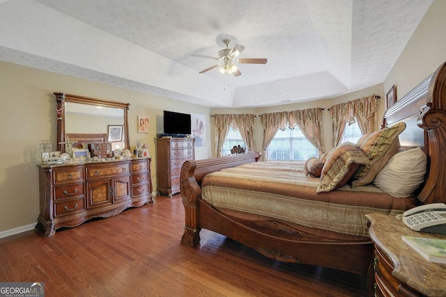 bedroom with ceiling fan, a tray ceiling, wood-type flooring, and a textured ceiling