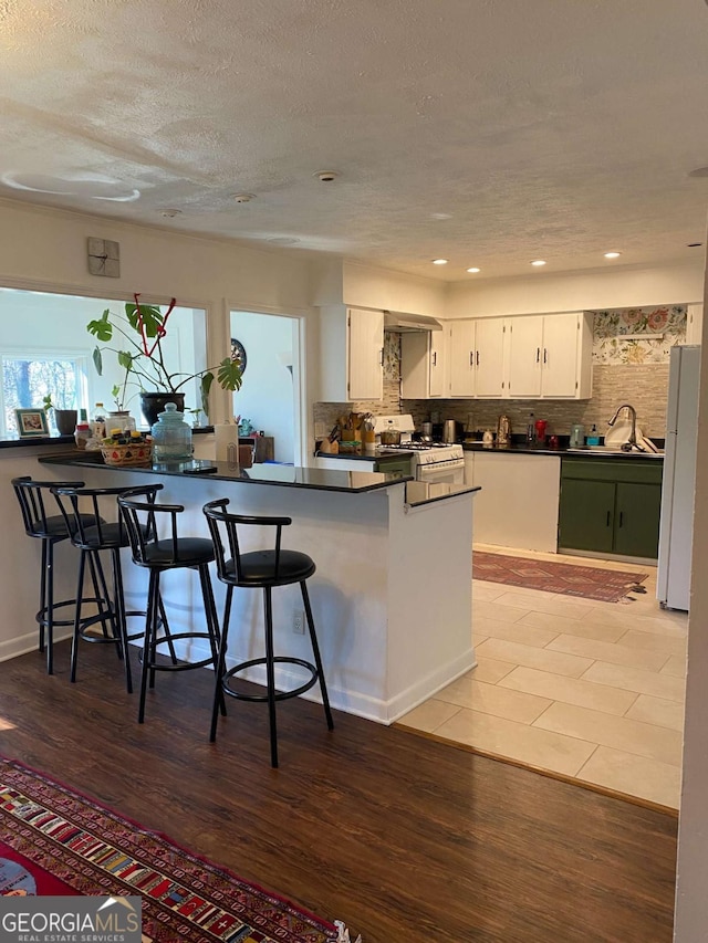 kitchen with kitchen peninsula, white cabinets, hardwood / wood-style flooring, white appliances, and backsplash