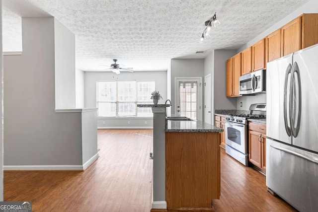 kitchen with sink, appliances with stainless steel finishes, an island with sink, a textured ceiling, and dark hardwood / wood-style flooring