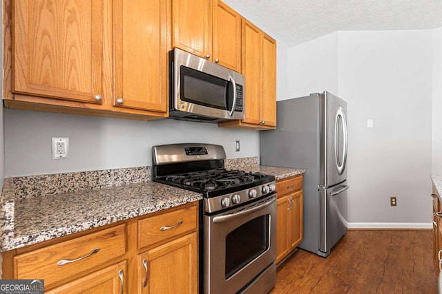 kitchen with stone countertops, dark hardwood / wood-style floors, a textured ceiling, and appliances with stainless steel finishes