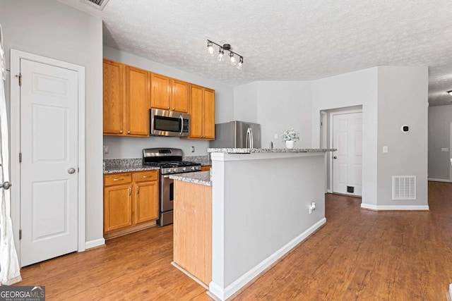 kitchen featuring stainless steel appliances, a center island, light stone countertops, a textured ceiling, and light wood-type flooring