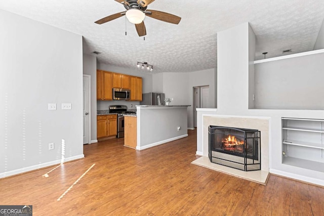 unfurnished living room featuring ceiling fan, a fireplace, a textured ceiling, and light wood-type flooring