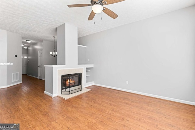 unfurnished living room featuring a multi sided fireplace, wood-type flooring, ceiling fan with notable chandelier, and a textured ceiling