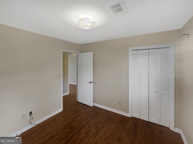 unfurnished bedroom featuring a textured ceiling, dark hardwood / wood-style flooring, and a closet