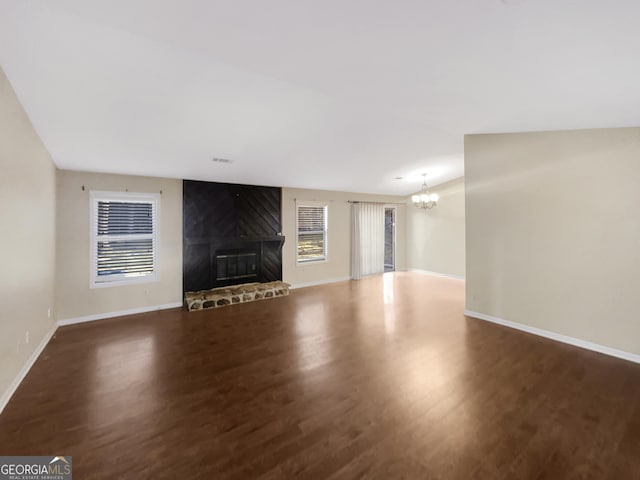 unfurnished living room with an inviting chandelier, a large fireplace, plenty of natural light, and dark hardwood / wood-style floors