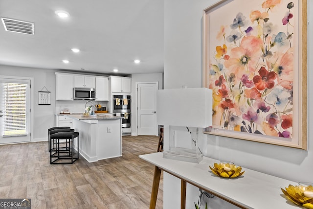 kitchen with visible vents, a breakfast bar area, light wood-style flooring, appliances with stainless steel finishes, and white cabinetry