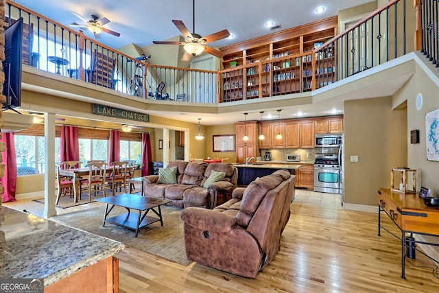 living room with sink, light hardwood / wood-style floors, ceiling fan, and a high ceiling