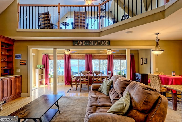 living room featuring ceiling fan, light wood-type flooring, and a towering ceiling