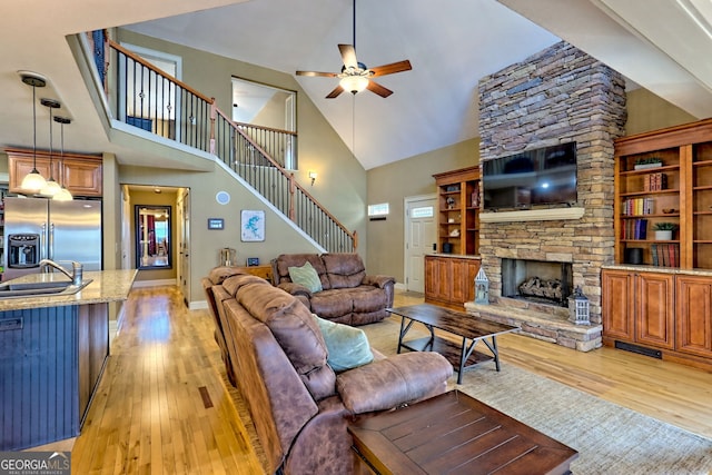 living room with sink, ceiling fan, high vaulted ceiling, a fireplace, and light wood-type flooring