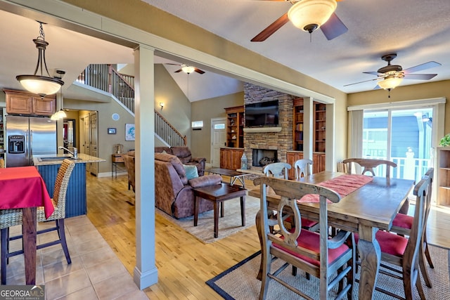 dining space with ceiling fan, a stone fireplace, sink, and light wood-type flooring