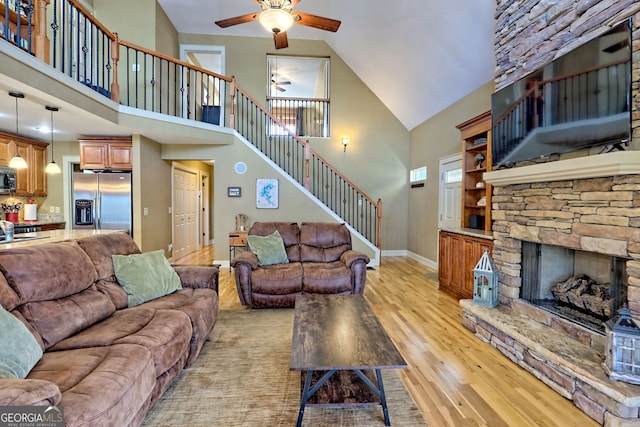 living room featuring ceiling fan, a stone fireplace, light hardwood / wood-style floors, and a towering ceiling