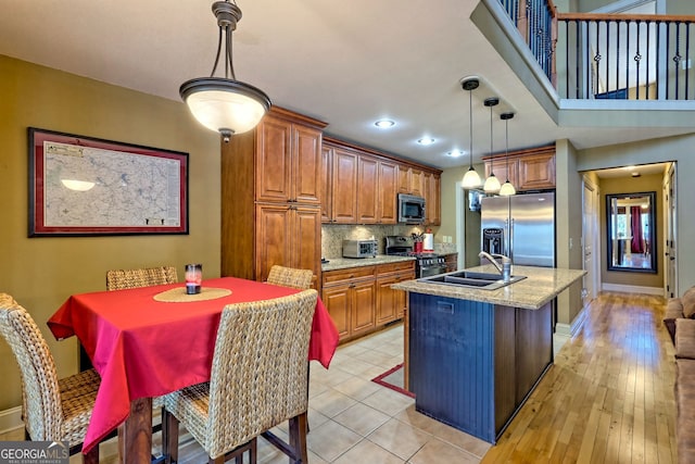 kitchen with appliances with stainless steel finishes, a kitchen island with sink, light stone counters, decorative backsplash, and decorative light fixtures