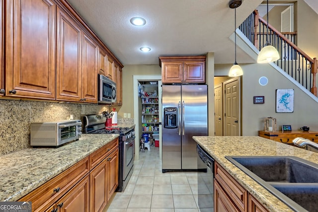 kitchen with light tile patterned flooring, sink, hanging light fixtures, stainless steel appliances, and light stone countertops