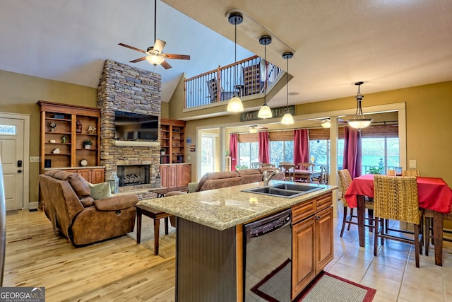 kitchen with pendant lighting, dishwasher, sink, light stone counters, and a center island with sink