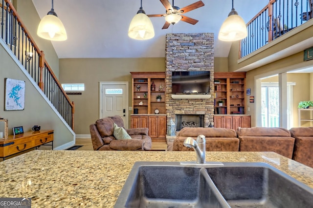 living room with sink, ceiling fan, hardwood / wood-style floors, a towering ceiling, and a fireplace