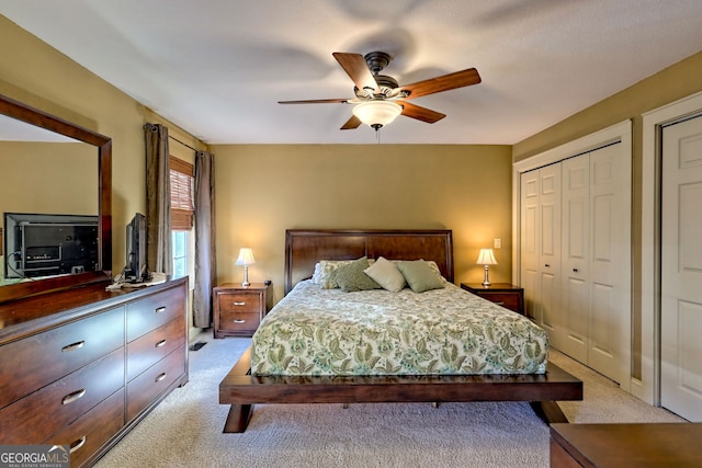 bedroom with ceiling fan, light colored carpet, and multiple closets