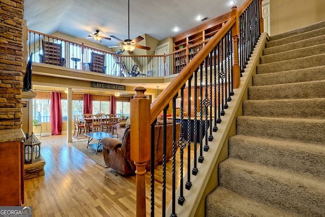 staircase featuring a towering ceiling, wood-type flooring, and ceiling fan