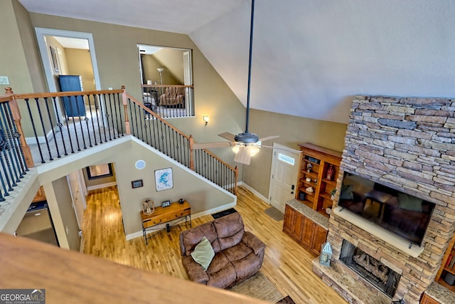 living room with ceiling fan, a stone fireplace, lofted ceiling, and light wood-type flooring