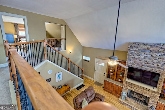 living room featuring a stone fireplace, vaulted ceiling, ceiling fan, and light wood-type flooring