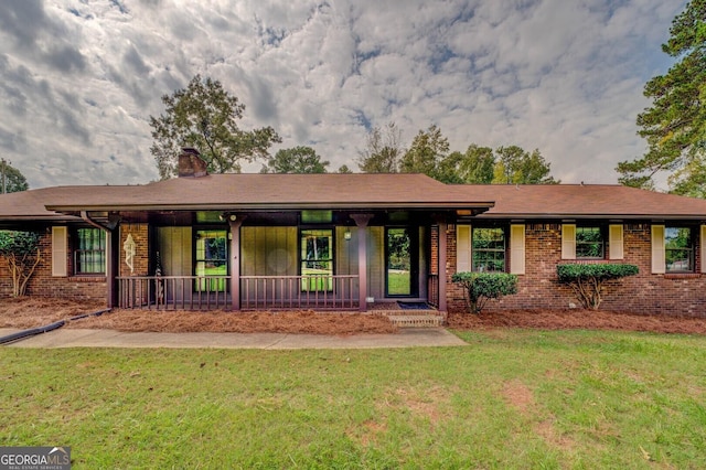 ranch-style home featuring covered porch, a front yard, a chimney, and brick siding