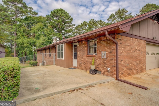 view of side of property featuring a garage, brick siding, and fence